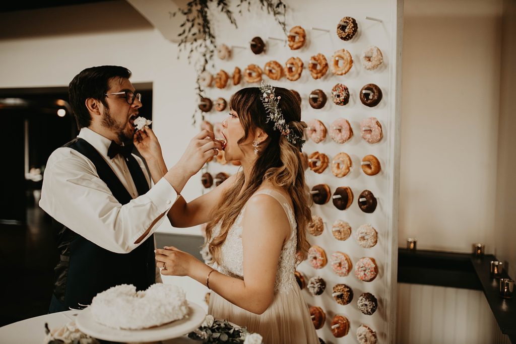 bride and groom feed each other donuts